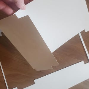 Puede incluir: Una tarjeta blanca con un dise&ntilde;o recortado, que muestra una tarjeta blanca m&aacute;s peque&ntilde;a con un dise&ntilde;o recortado. La tarjeta m&aacute;s peque&ntilde;a se levanta para revelar la tarjeta m&aacute;s grande.