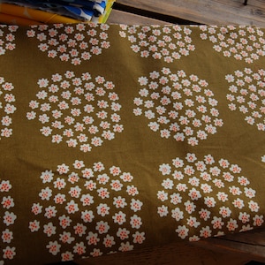 May include: A brown fabric with a repeating pattern of white circles with small orange dots. The fabric has a subtle texture.