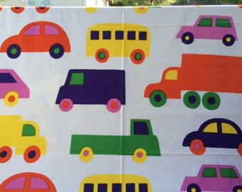 Può includere: Un tessuto bianco con un motivo ripetuto di veicoli colorati, tra cui auto, camion e autobus arancioni, gialli, viola e verdi. Ogni veicolo è raffigurato in uno stile grafico piatto con ruote e finestrini a contrasto in vari colori vivaci.