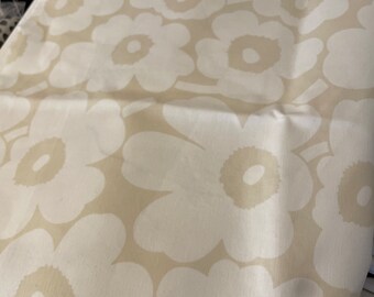 Puede incluir: Tela beige con un patrón floral blanco. Las flores son grandes y tienen una forma simple y redondeada.