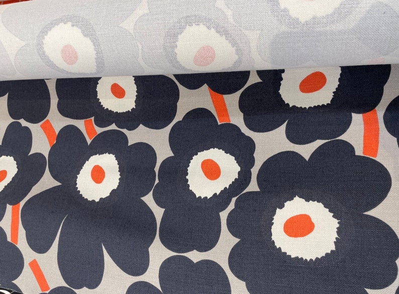 May include: A close-up of a fabric with a repeating pattern of large, navy blue flowers with white centers and orange accents on a light gray background.
