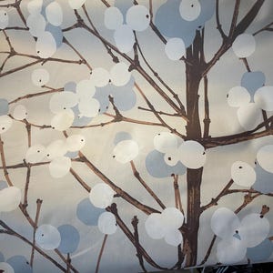 Op de afbeelding: Stof met een herhalend patroon van gestileerde takken en bessen. De takken zijn bruin en de bessen zijn wit en lichtblauw tegen een lichte achtergrond. Het ontwerp heeft een moderne, botanische uitstraling.