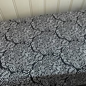 May include: Black and white fabric with a repeating pattern of stylized flowers. The flowers are made up of small, white lines that create a swirling, organic effect.