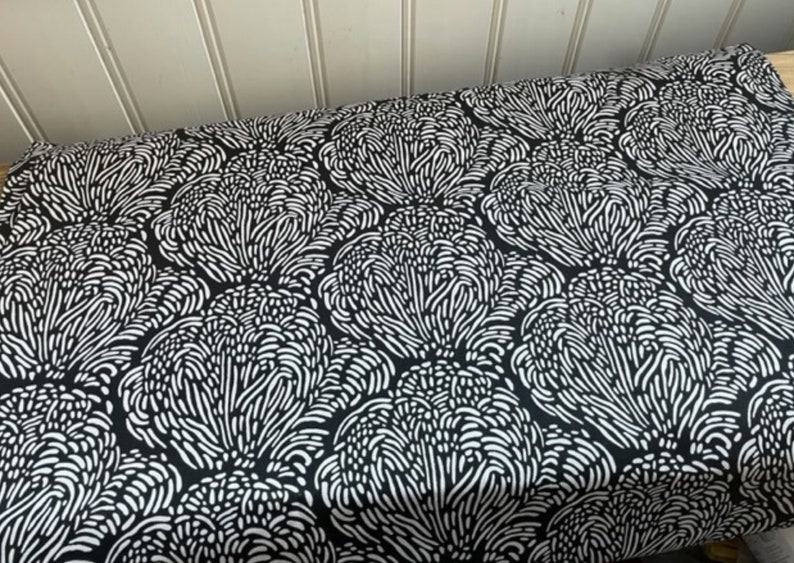 May include: Black and white fabric with a repeating pattern of stylized flowers. The flowers are made up of small, white lines that create a swirling, organic effect.