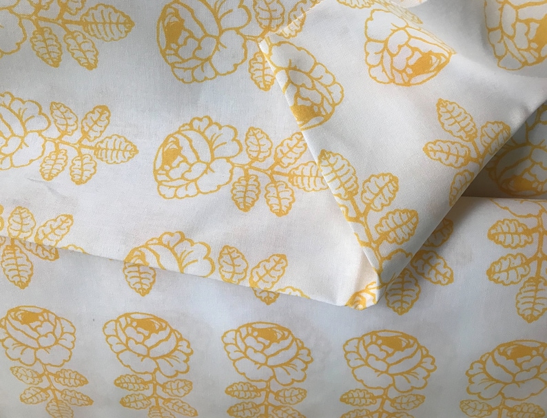 May include: White fabric with a yellow floral pattern. The fabric features a repeating design of stylized roses and leaves.