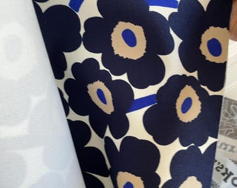 May include: A fabric sample featuring a large floral pattern. The design showcases navy blue flowers with tan centers and blue accents against a white background. The fabric is folded, revealing a plain white underside.