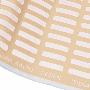 May include: Close-up of a beige fabric with a white geometric pattern. The fabric has the text "ALVAR AALTO DESIGN "SIENA" printed on the bottom edge.