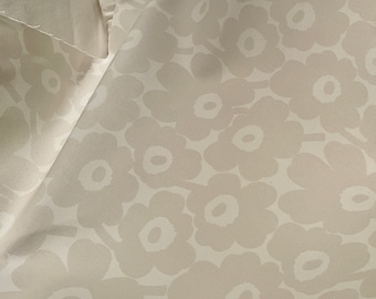 May include: Close-up of a white fabric with a repeating pattern of beige stylized flowers.