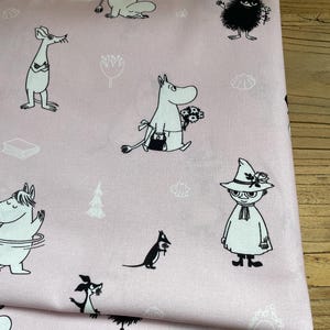 Könnte beinhalten: Hellrosa Stoff mit einem sich wiederholenden Muster aus schwarz-weißen Cartoonfiguren. Der Stoff zeigt verschiedene Charaktere, Blumen und baumartige Designs. Der Stoff ist gefaltet und zeigt seine Textur und die Kontinuität des Musters.