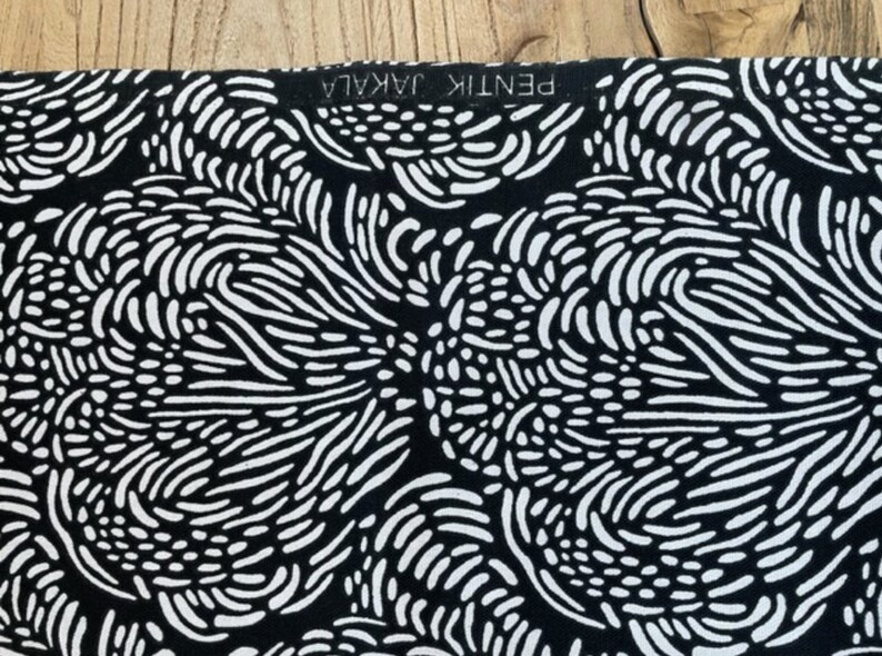 May include: Black and white fabric with a repeating pattern of abstract swirls and lines. The fabric has a label that reads "PENTIK JAKALA".
