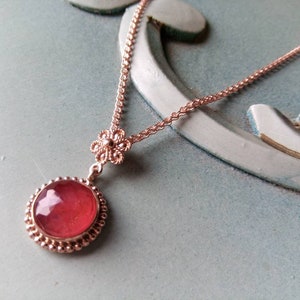 May include: A rose gold necklace featuring a dainty flower charm and a large, round, pink gemstone pendant.