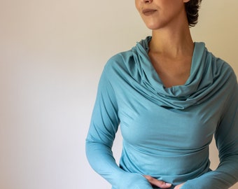 Puede incluir: Una mujer con una camisa de manga larga de color azul turquesa con cuello de pico y una falda negra.