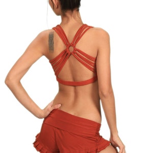 Puede incluir: Un sujetador deportivo de color óxido con espalda cruzada y un detalle circular en el centro. El sujetador se combina con una falda de color óxido con volantes.