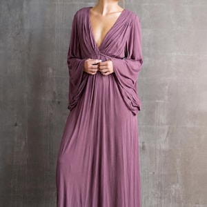 May include: A floor-length mauve maxi dress featuring a deep V-neckline, gathered fabric at the bodice, and long, loose-fitting kimono-style sleeves. The garment has a flowing, pleated skirt that extends to the floor, creating a draped silhouette.