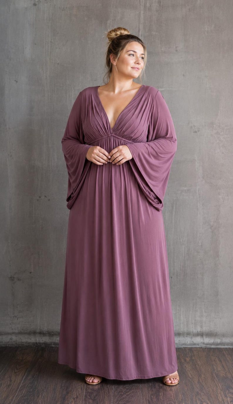 May include: A floor-length mauve maxi dress featuring a deep V-neckline with gathered fabric detailing at the bodice and wide, flowing bell sleeves. The garment has a fitted waistline that transitions into a loose, floor-sweeping skirt.