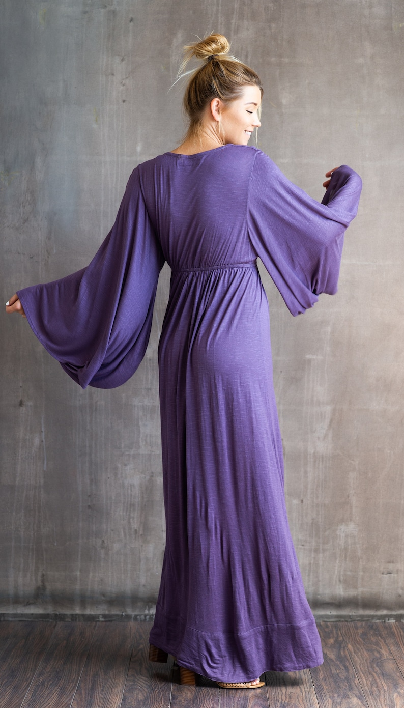 May include: A floor-length purple dress featuring long, wide bell sleeves and a gathered waistline. The garment has a V-neckline and a flowing, loose-fitting skirt that extends to the floor, crafted from a soft, solid-colored fabric.