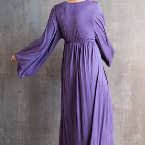 May include: A floor-length purple dress featuring long, wide bell sleeves and a gathered empire waistline. The garment has a simple round neckline and a flowing, loose skirt that extends to the floor, crafted from a soft, solid-colored fabric.