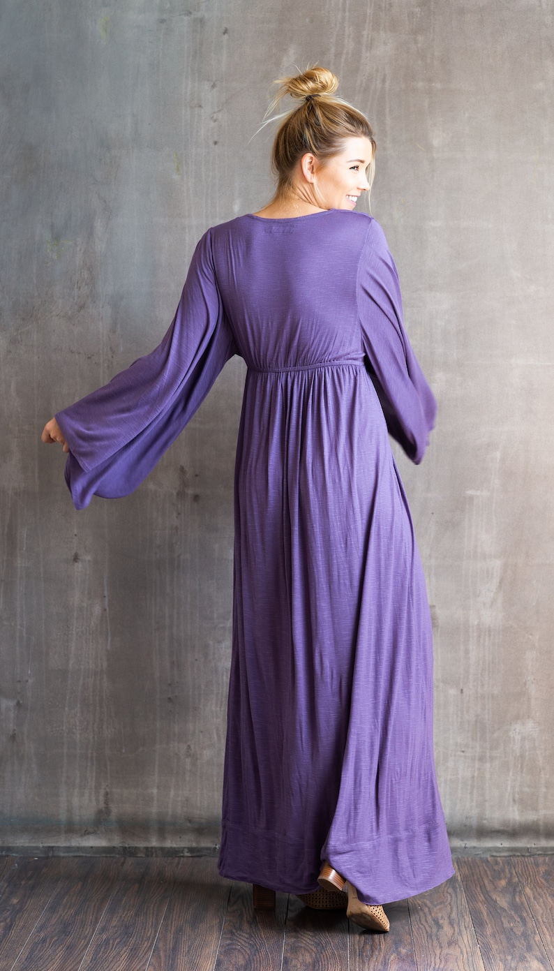 May include: A floor-length purple dress featuring long, wide bell sleeves and a gathered empire waistline. The garment has a simple round neckline and a flowing, loose skirt that extends to the floor, crafted from a soft, solid-colored fabric.