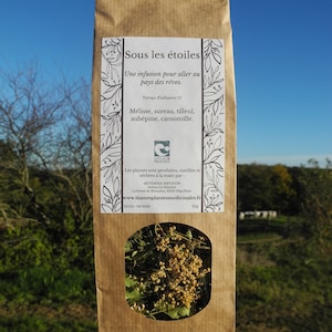 Peut inclure: Un sachet en papier kraft avec une fenêtre transparente montrant des herbes séchées. Le sachet est étiqueté "Sous les étoiles" et liste les ingrédients : "Mélisse, sureau, tilleul, aubépine, camomille". Le sachet comprend également le nom de la marque "Nature & Progrès" et le site web "www.tisanesplantesmedicinales.fr".