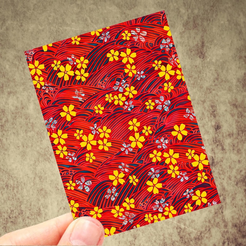 May include: A rectangular card with a vibrant red background featuring a repeating pattern of yellow flowers and stylized wave-like lines. The card is held by a hand, showcasing the intricate design and color contrast.