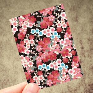 May include: A rectangular card with a floral pattern. The design features pink, red, white, and blue flowers on a black background. The flowers have gold accents and are arranged in a dense, all-over pattern.