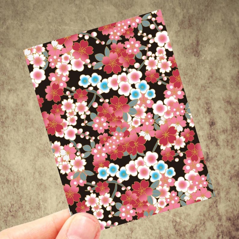 May include: A rectangular card with a floral pattern. The design features pink, red, white, and blue flowers on a black background. The flowers have gold accents and are arranged in a dense, all-over pattern.