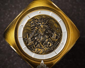 May include: A gold-toned metal dice with a white face featuring a detailed illustration of a mythical creature with horns and weapons. The dice has numbers 1 through 6 around the edge.