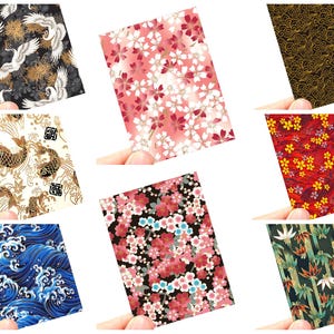 May include: A collection of Japanese-style patterned cards, each held by a hand. Designs include cranes, cherry blossoms, koi fish, waves, and bamboo. Colors range from black and gold to red and pink.