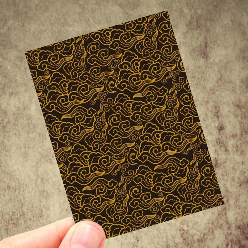 May include: A rectangular card featuring a repeating pattern of swirling gold cloud designs on a dark brown background. The card is held by a hand, showcasing the intricate details of the pattern. The design evokes a sense of traditional Asian art.