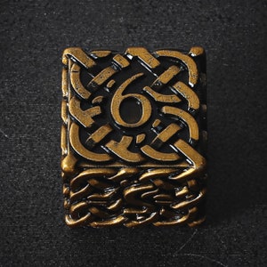 May include: A rectangular, bronze-colored metal object with a Celtic knot design and the number "6" in the center. The background is black, and the object has a textured appearance.