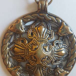 Könnte beinhalten: Eine goldfarbene Halskette mit einem runden Anhänger, der ein keltisches Knotenmuster und vier stilisierte Tierköpfe zeigt. Der Anhänger ist an einer Kette mit einem Federringverschluss befestigt.