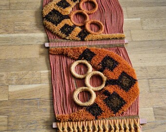 A long handwoven picture tapestry in beautiful rust-colored colors with wooden rings,