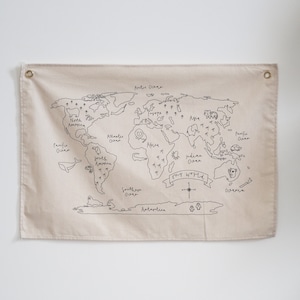 May include: A beige canvas wall tapestry featuring a black line drawing of a world map. The map includes the continents, oceans, and the text "Our World".