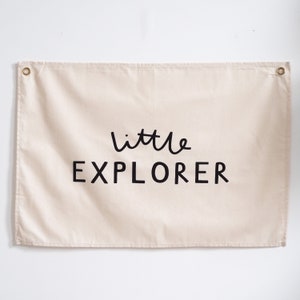May include: A beige canvas wall tapestry with black text that reads "little EXPLORER".