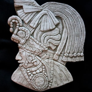 Puede incluir: Una escultura en relieve de yeso blanco de una persona que lleva un tocado con intrincados detalles. La escultura está de perfil y se ve la cara de la persona.