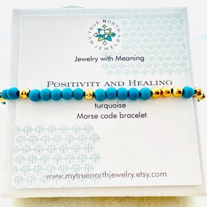 Könnte beinhalten: Ein türkisfarbenes Morsecode-Armband mit goldfarbenen Perlen. Das Armband wird auf einer weißen Karte mit dem Text "POSITIVITY AND HEALING" und "Jewelry with Meaning" präsentiert. Die Website-Adresse www.mytruenorthjewelry.etsy.com ist ebenfalls sichtbar.