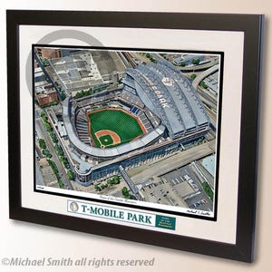 May include: Framed aerial view of T-Mobile Park, home of the Seattle Mariners, with a green baseball field, gray stadium, and surrounding city infrastructure. The artwork is in a black frame with a white mat.