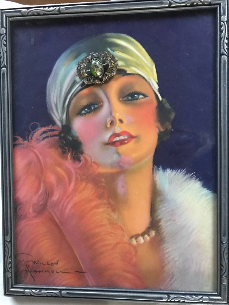 Puede incluir: Un retrato enmarcado de una mujer con un turbante blanco con un broche de joyas, un boa de plumas rosa y un cuello de piel blanca. La mujer tiene el pelo oscuro y mira hacia arriba. El retrato est&aacute; firmado "Wilson" en la esquina inferior izquierda.