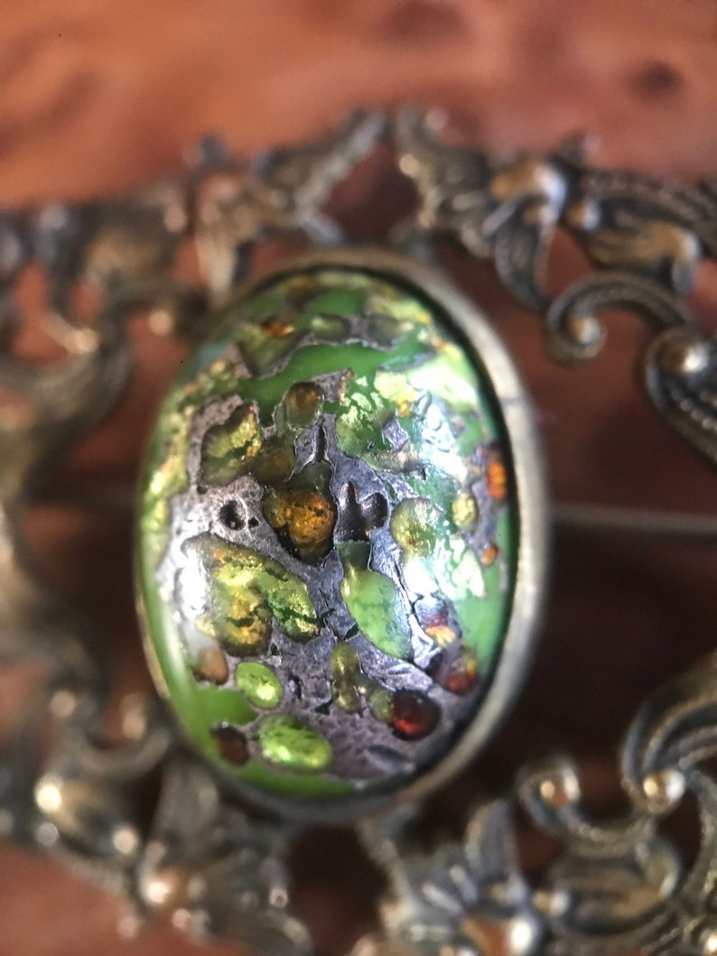 Puede incluir: Un broche vintage con un cabuj&oacute;n de esmalte verde, plateado y dorado, engastado en un marco de plata adornado.