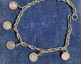May include: A silver chain bracelet with multiple silver coin charms. The coins have different designs, including a profile of a person and an image of an American Indian.