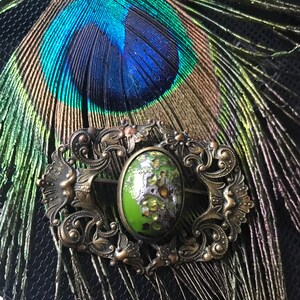 Puede incluir: Un broche vintage con un cabuj&oacute;n ovalado verde y plateado engastado en un marco de metal dorado adornado.