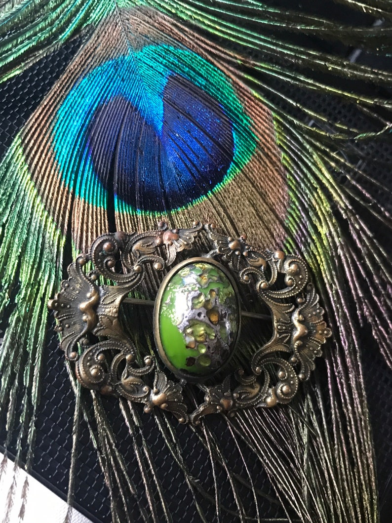 Puede incluir: Un broche vintage con un cabuj&oacute;n ovalado verde y plateado engastado en un marco de metal dorado adornado.
