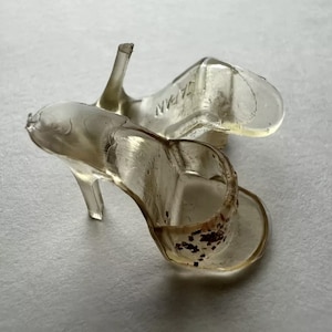 May include: A pair of clear plastic high-heeled shoes with a gold-colored trim around the opening of the shoe. The shoes are made in Japan.