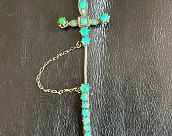 May include: A silver and turquoise sword brooch with a chain attached. The sword is decorated with turquoise stones and has a pointed tip.