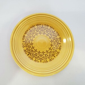May include: A yellow ceramic plate with a brown floral design. The plate has a raised rim and a slightly scalloped edge.