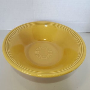 May include: A yellow ceramic bowl with a glossy finish. The bowl has a wide rim with concentric grooves and a central circular design. The bowl is a bright, solid yellow color.