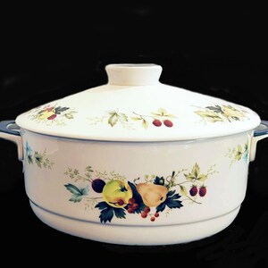 May include: White ceramic casserole dish with a lid and two handles. The dish is decorated with a floral pattern featuring green leaves, red berries, and yellow and red fruit.