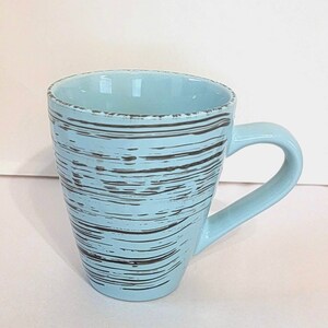 May include: A light blue ceramic mug with a black and white striped design. The mug has a handle and a rounded shape.
