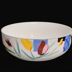 May include: White ceramic bowl with a colourful abstract floral design featuring yellow, blue, pink, and brown accents.