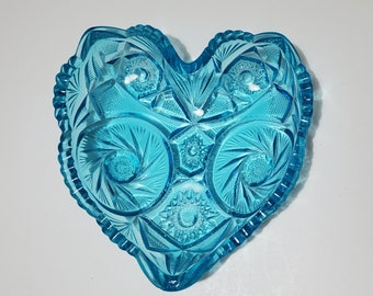 May include: A heart-shaped glass dish with a blue, iridescent finish. The dish has a cut-glass design with intricate patterns.